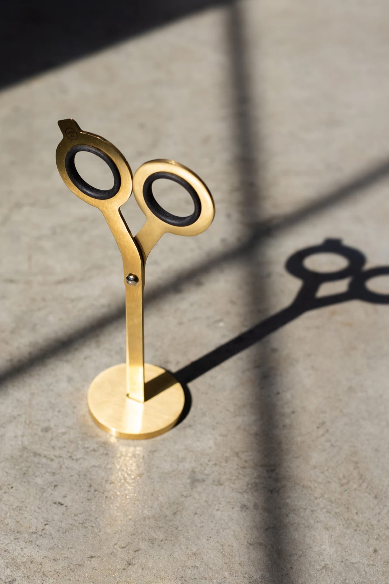 Brass scissors with geometric design, black steel finger holes, and included upright brass stand.