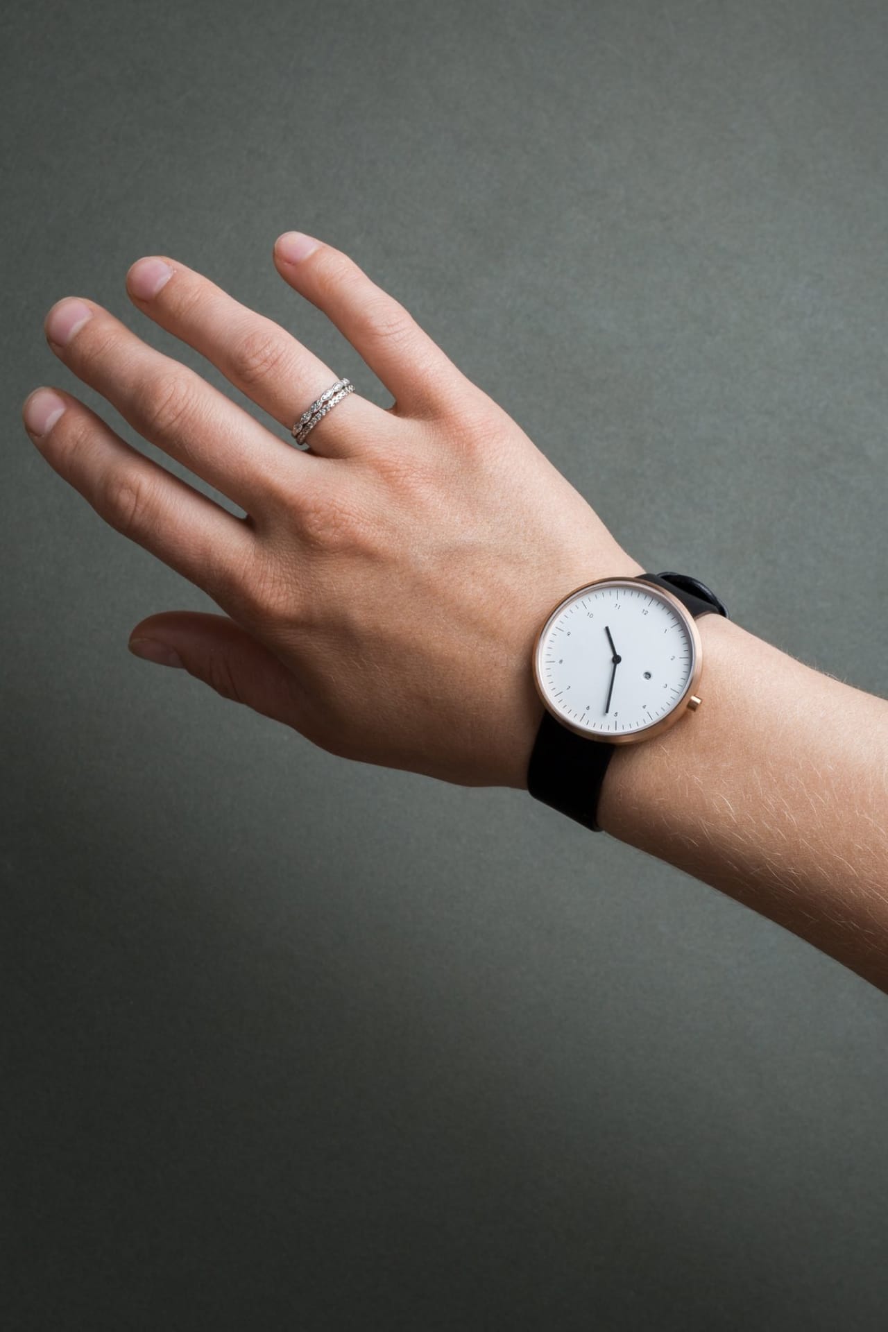 Arm modeling wristwatch with black leather band, white watch face, thin watch hands, and fine time markings.