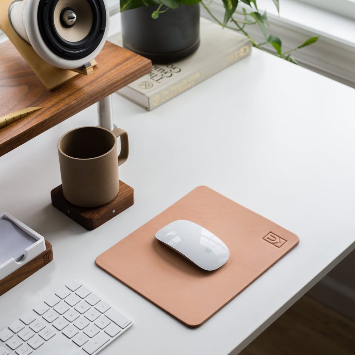 Natural leather mouse pad on white desk next to porcelain mug and keyboard.