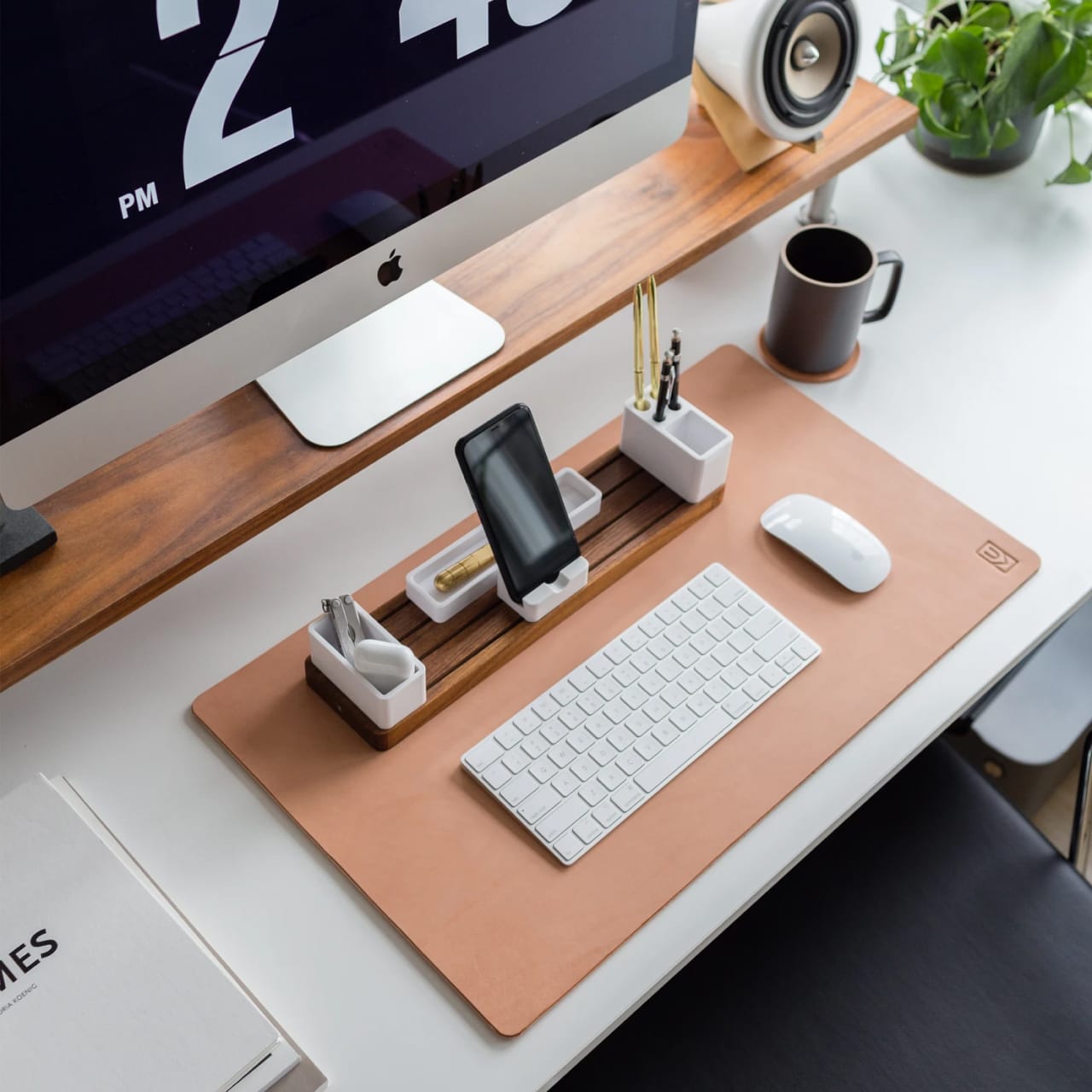 Desk with leather desk pad, walnut desk organizer, wireless keyboard and mouse, and porcelain mug.