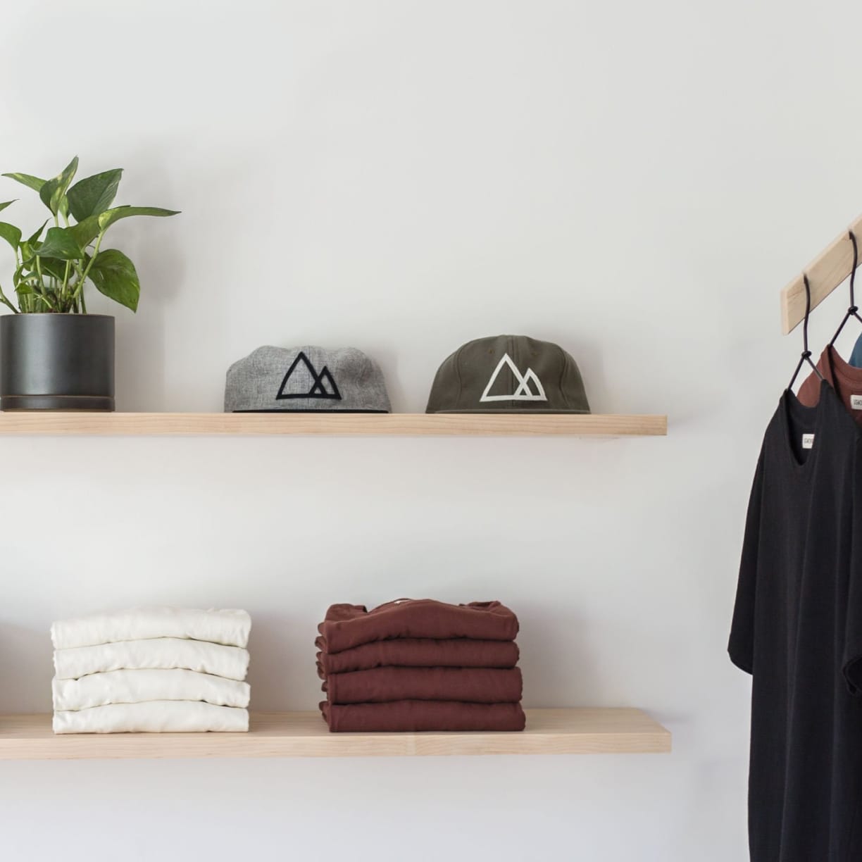 Wooden shelf with gray and olive drab green baseball caps, next to wooden clothes hanger with sweaters.