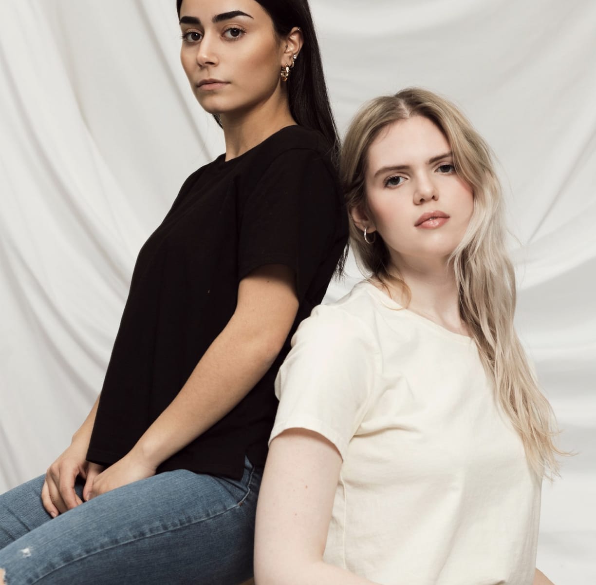 Two models wearing women's black cotton crewneck tee and off-white cotton crewneck tee.