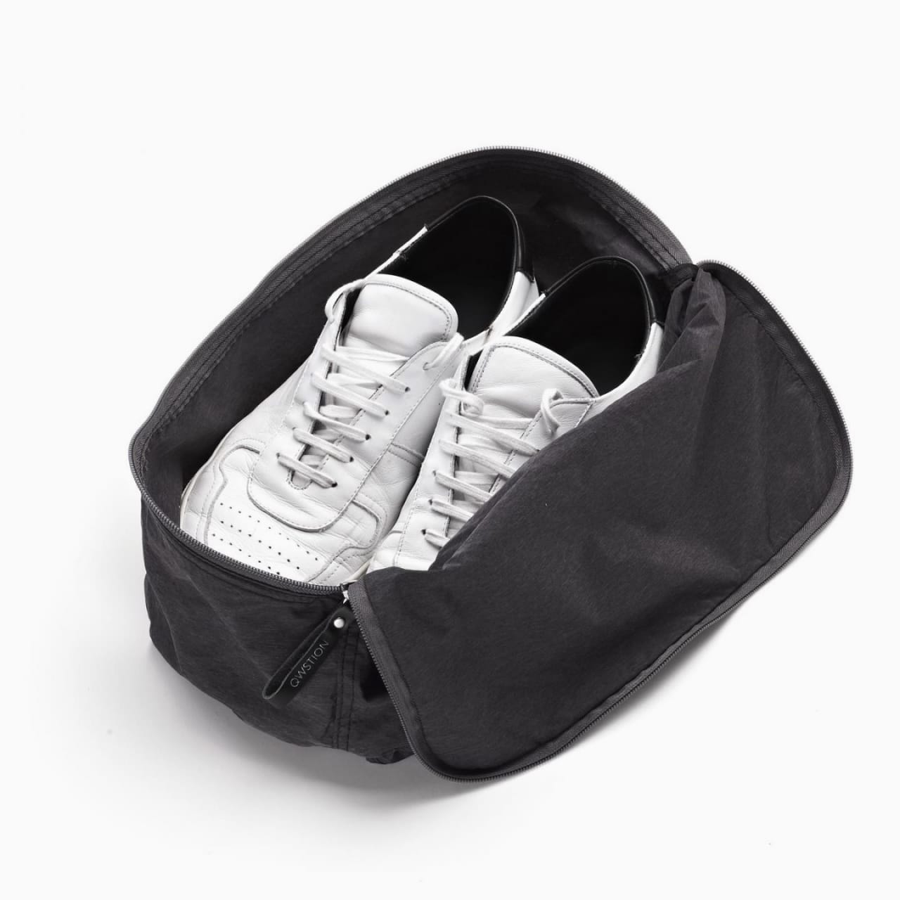 Black fabric shoe bag with zipper around 3 sides, holding pair of white sneakers.