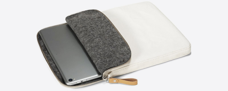 White canvas laptop sleeve with gray felt interior, silver zipper, and tan leather zipper pull.