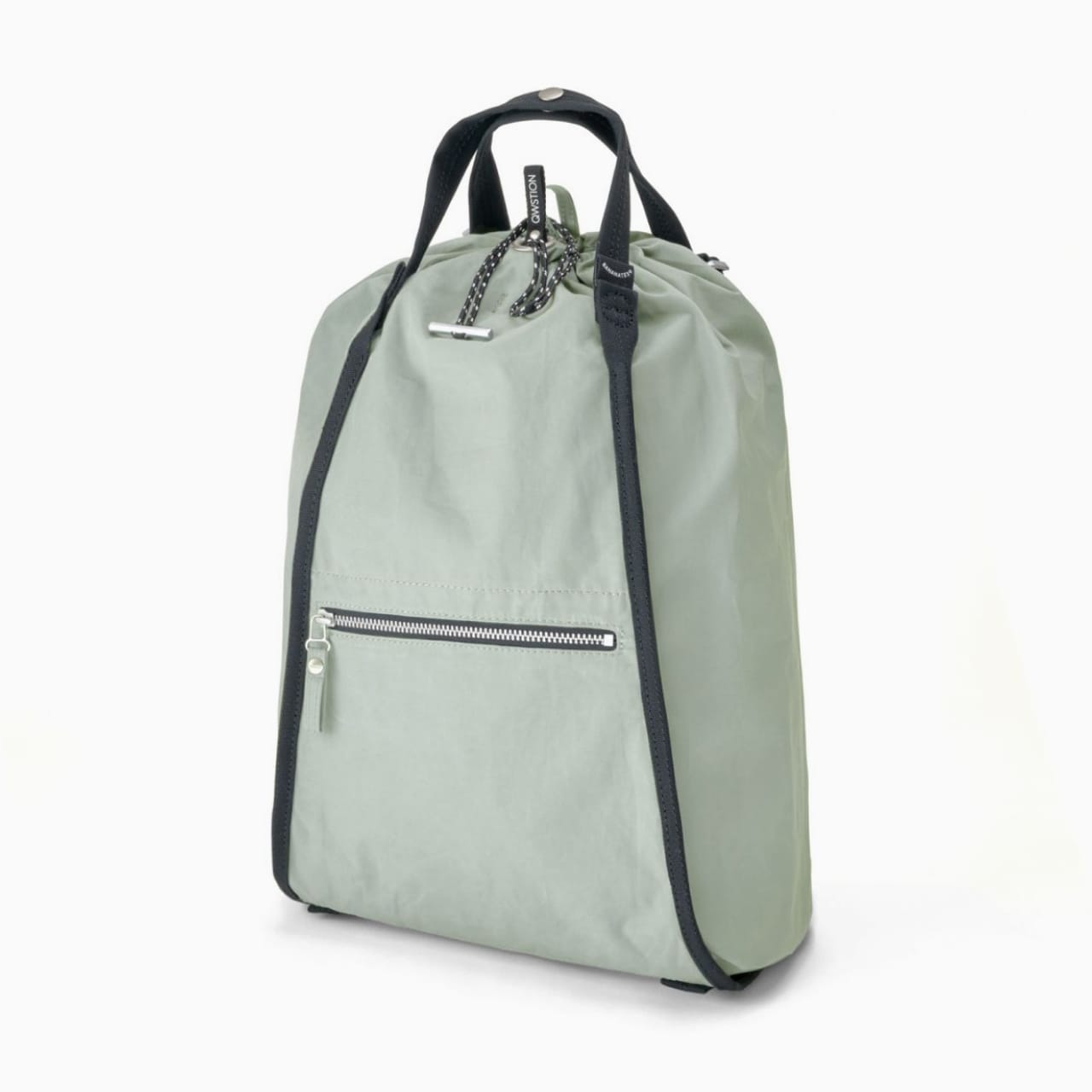Light green canvas bag with black straps, handle, front zipper pouch, and drawstring top.