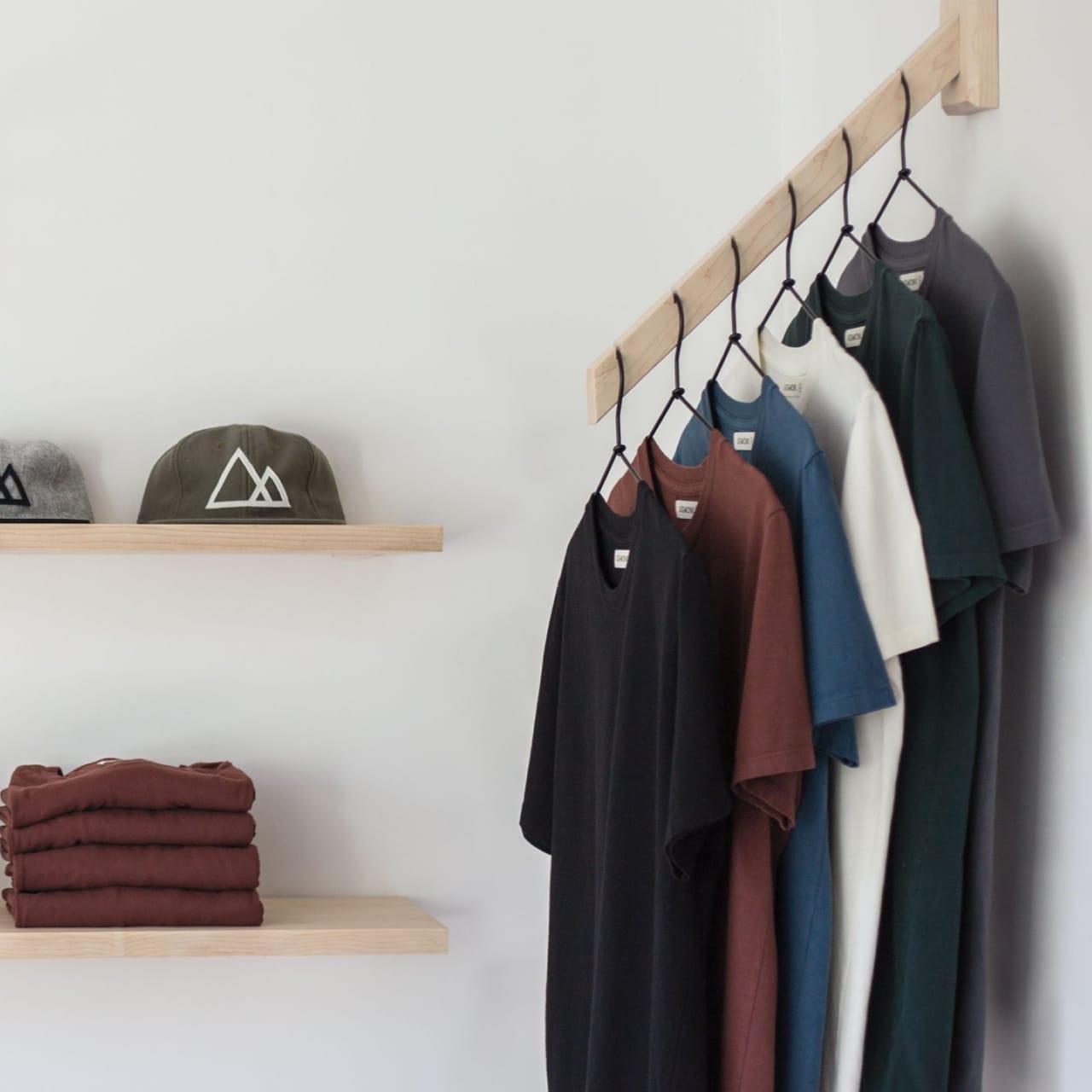 Hats and sweaters on wood shelves next to various colors of t-shirts on hangers.
