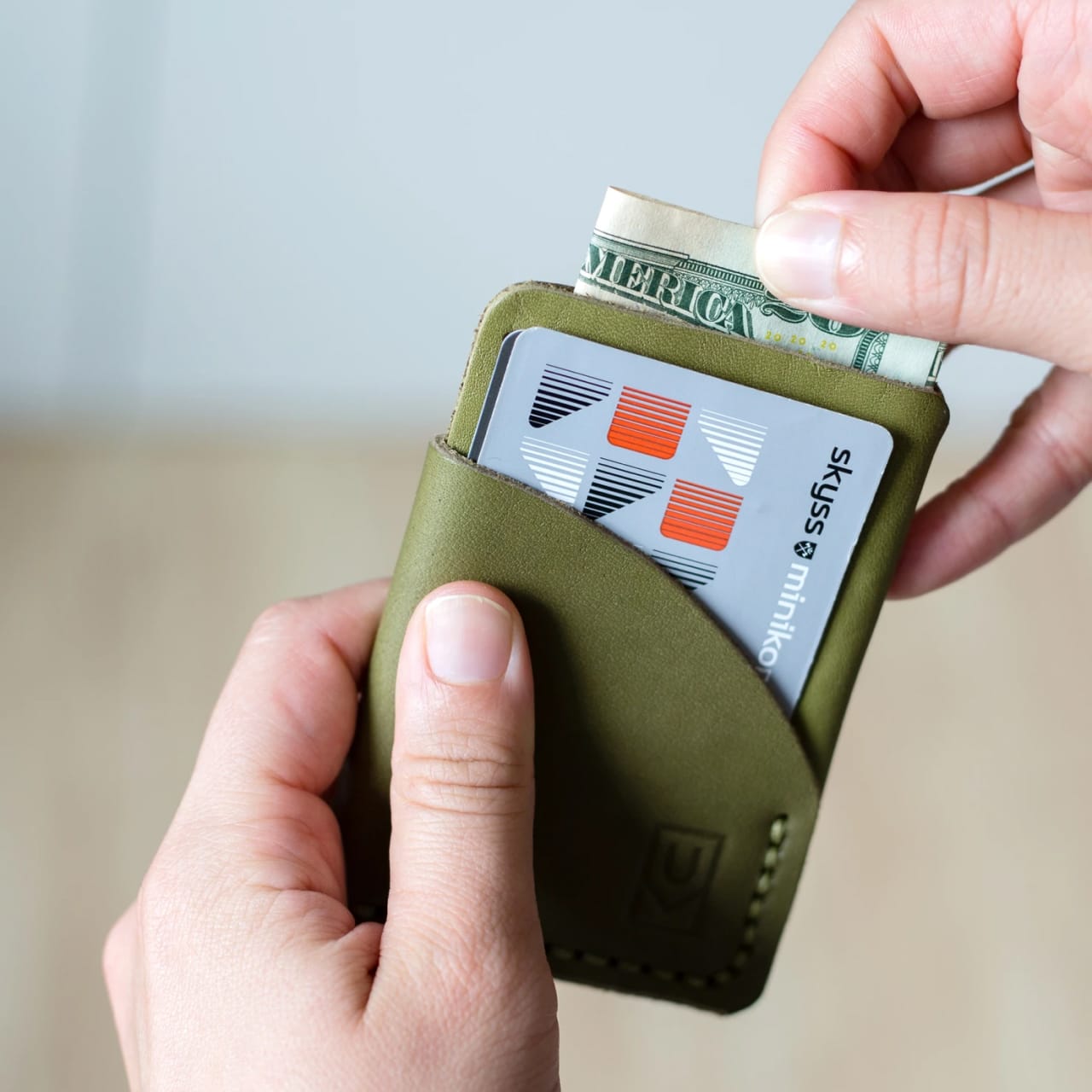 Model putting folded cash into slim card holder olive leather wallet with hand stitching.
