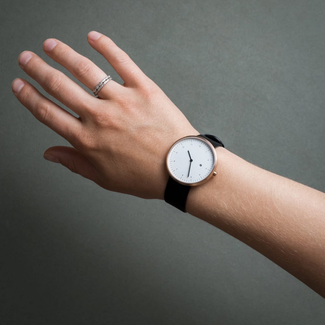 Model wearing minimalist watch with black wristband and white watch face.