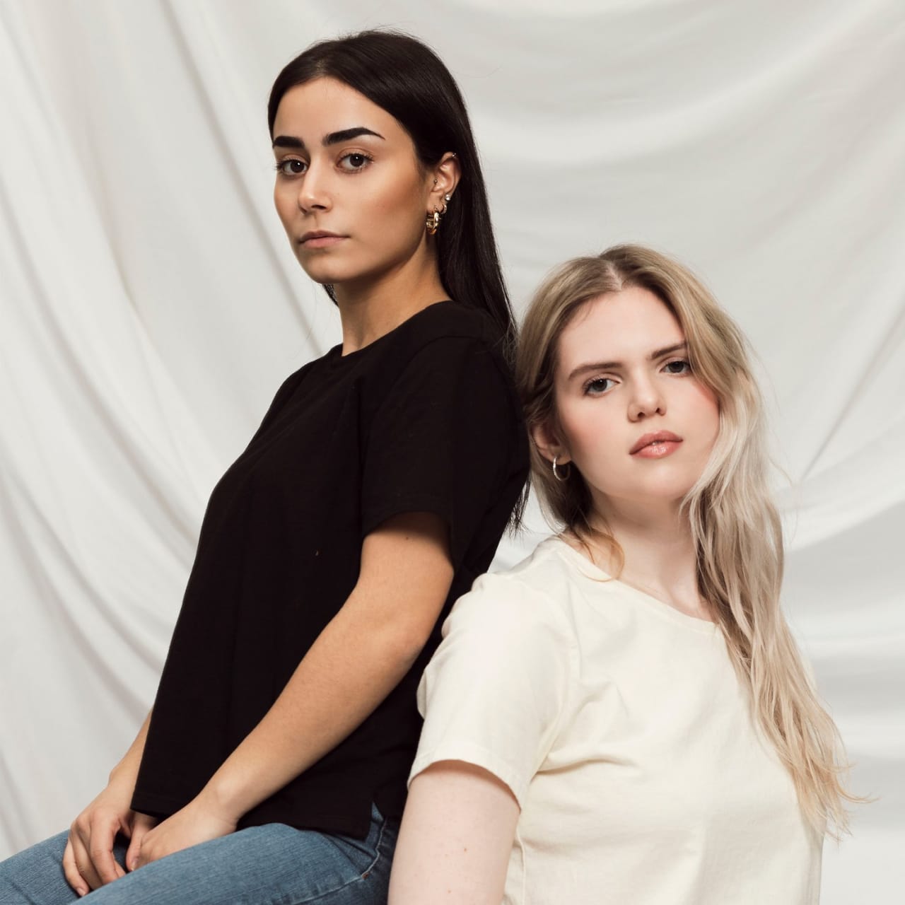 Models sitting back to back, wearing Basic Tee in black and bone.